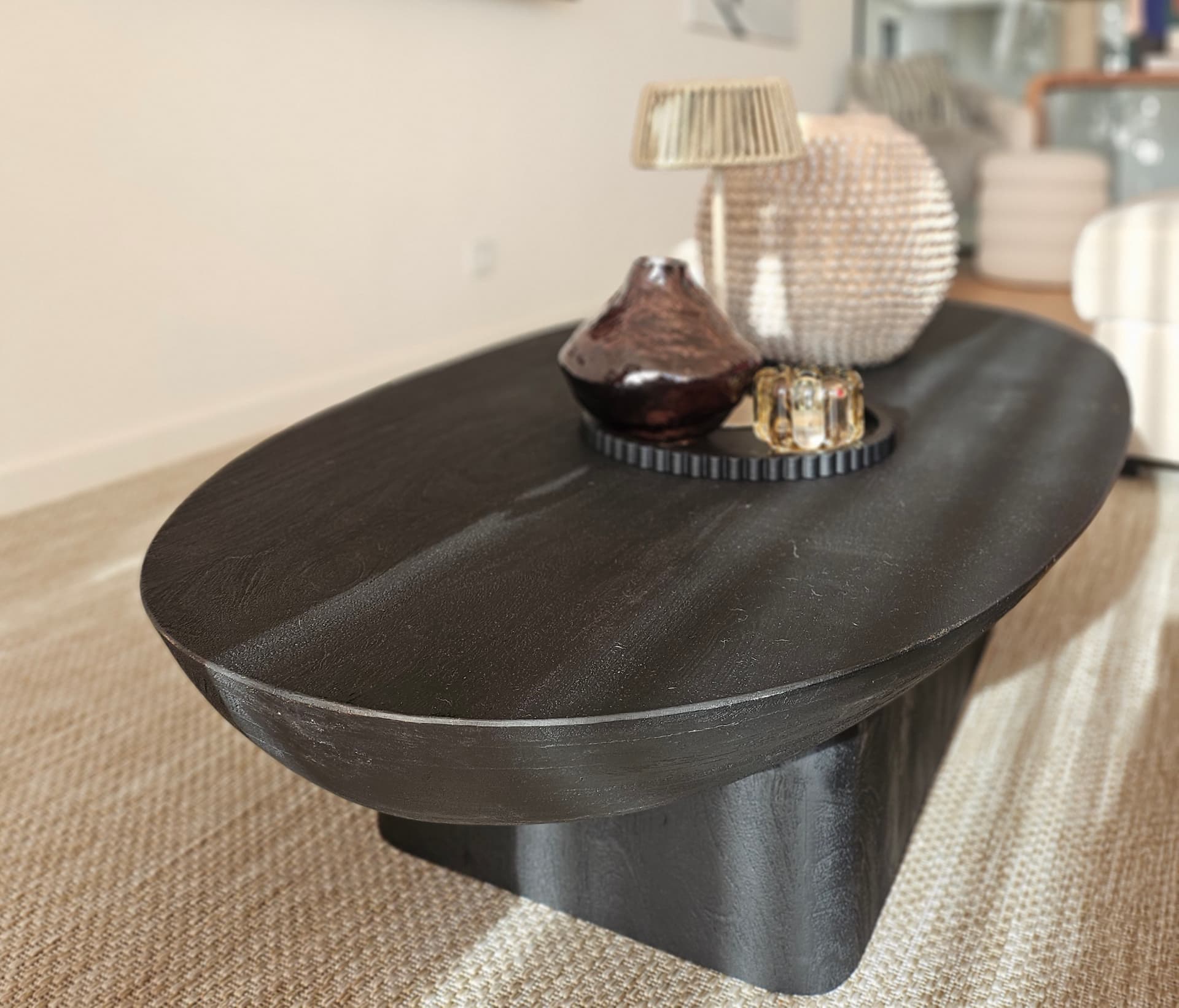 Sculptural dark wood coffee table styled with ceramics on a woven rug